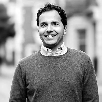 Portrait of a smiling founder in a sweater and collared shirt, outdoors.