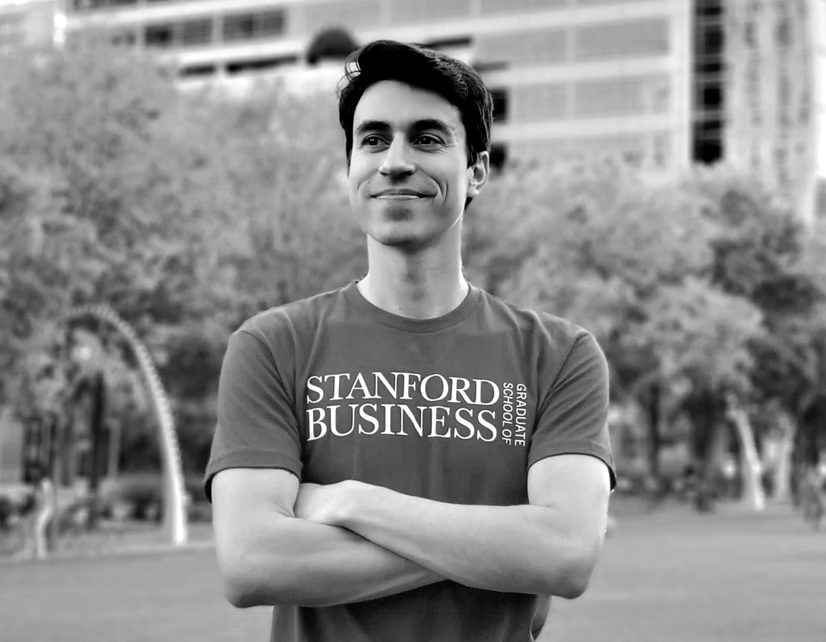 Founder with arms crossed in a park, wearing a Stanford Business T-shirt.