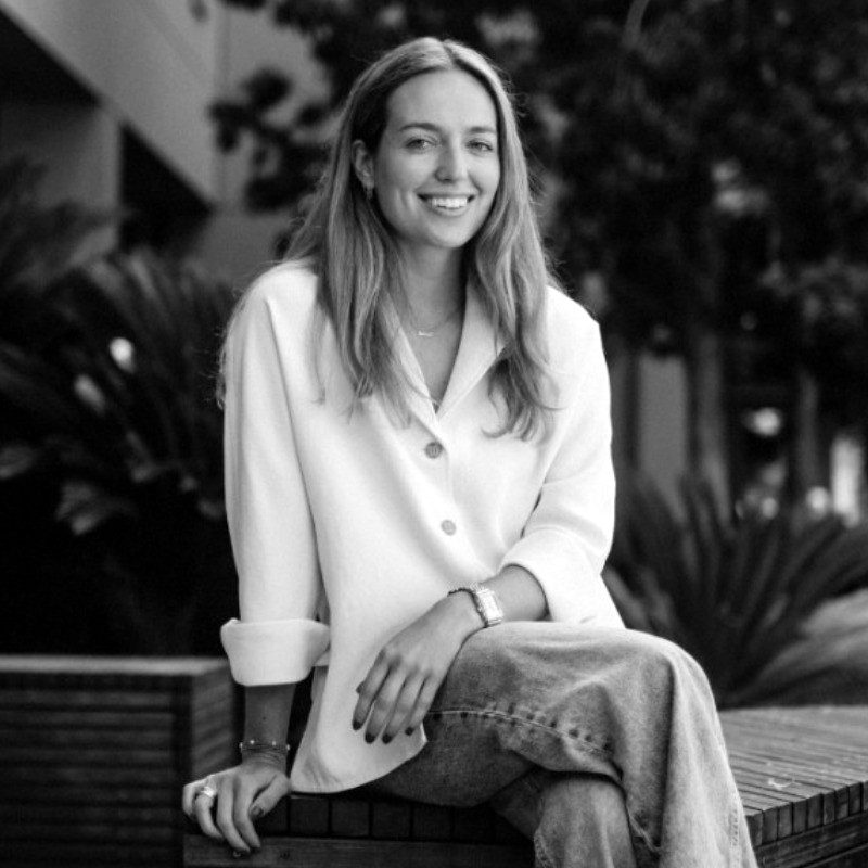 Portrait of a smiling founder in a white shirt, sitting outdoors.