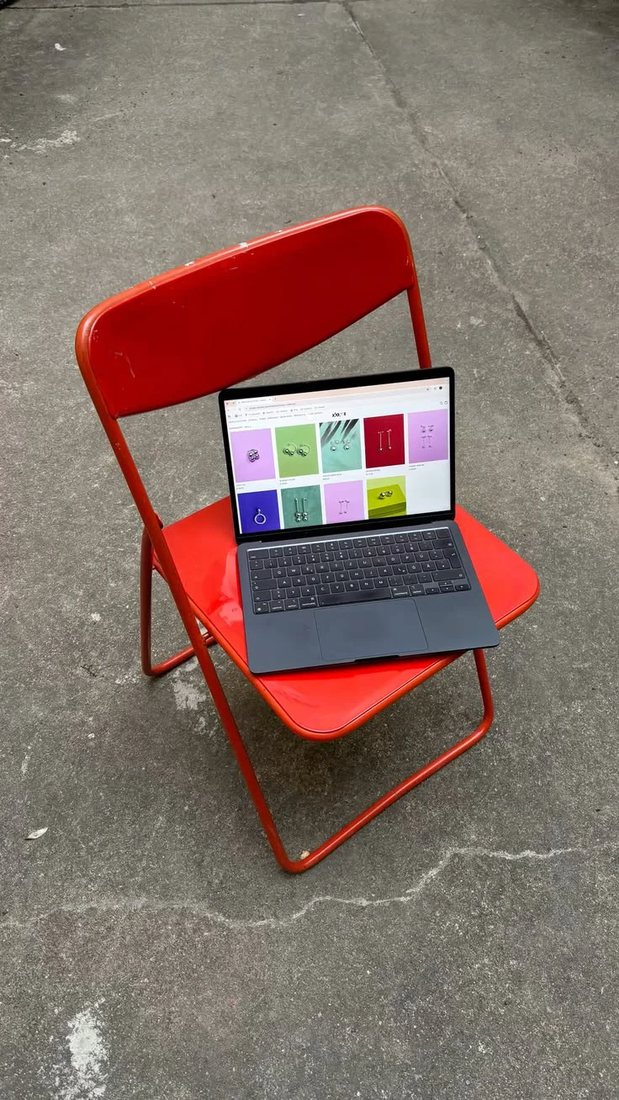 An open laptop showing a colourful product grid, resting on a red folding chair on concrete.